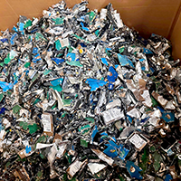 A large cardboard box filled with a pile of crushed and shredded electronics components, including circuit boards and metallic pieces.