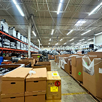 Large warehouse interior with high shelves and rows of stacked cardboard boxes and packages, industrial lighting overhead.